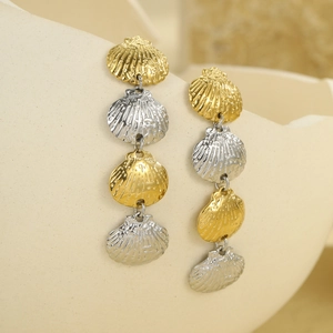 18k gold and silver scallop shell drop earrings hanging on a beige ceramic vase