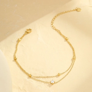 Detailansicht der doppellagigen goldenen Fußkette mit Perlen und einem Zirkonstein