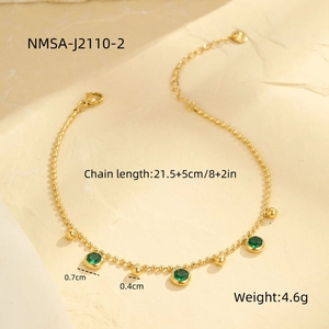 Detail of gold beaded anklet featuring emerald green gemstones on textured stone background