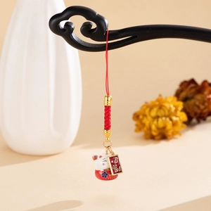 Detailed view of ceramic Maneki Neko charm with red woven cord and gold metal plaque