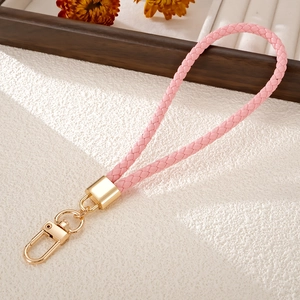 Pink hand-woven PU leather phone strap with gold-tone lobster clasp on textured background