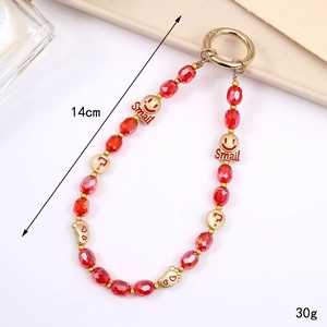 Red beaded phone charm strap with golden smile and heart pendants on cream surface