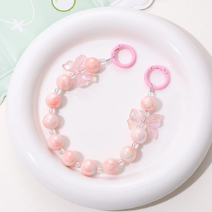 Pink pearlescent beaded phone strap with bow tie accent on white ceramic plate