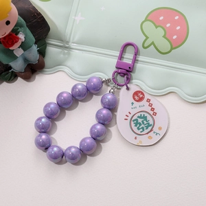 Macro shot of purple pearlescent beaded keychain with 'Get Rich' acrylic charm and metal hook
