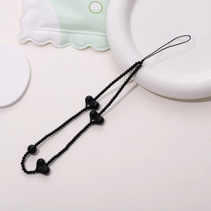 Detail of handmade black beaded phone strap with heart charms on ivory surface