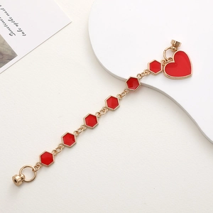 Détail d'une chaîne de téléphone dorée avec pendentifs cœur et hexagone en émail rouge