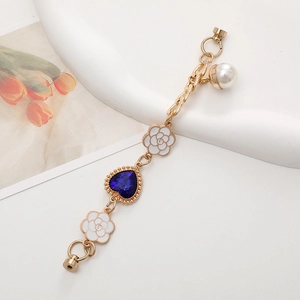 Goldenes Accessoire mit weißen Kamelienblüten und einem blauen Herz-Edelsteinanhänger