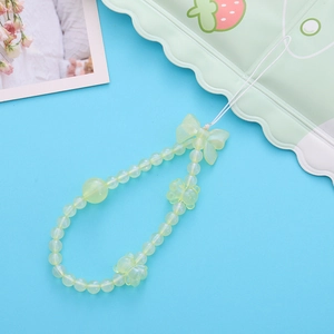 Détail de la dragonne de téléphone perlée vert clair avec breloques d'ours et de nœuds sur bleu