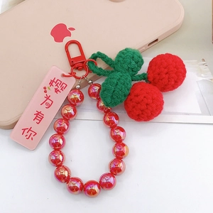 Macro detail of handmade crochet cherry charm with green leaves and red iridescent beads