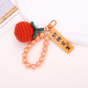 Close-up of hand-knitted orange persimmon keychain with colorful beads and metal hook
