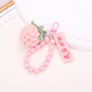 Handmade crochet pink strawberry keychain with pearl beads and acrylic tag on pink background