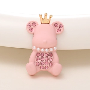 Détail d'un accessoire ours rose avec couronne dorée, perles et strass brillants