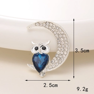 Macro shot of silver owl on crescent moon brooch with blue crystal heart and rhinestones