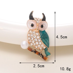Detailed close-up of a rhinestone owl brooch with green enamel wings and white pearl accent