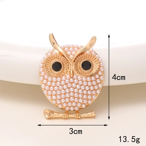 Detailed view of owl brooch with white pearls and black gemstone eyes on golden branch