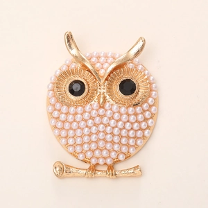 Golden owl brooch with white pearls and black gemstone eyes on a beige background