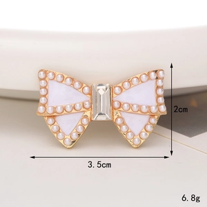 Vue détaillée d'une broche en forme de nœud avec perles, cadre doré et émail blanc