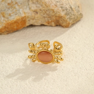 Anello granchio dorato con pietra occhio di gatto arancione su sfondo di sabbia