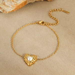 Detailed macro shot of irregular golden lava heart bracelet with inlaid pearl on sand rock