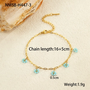 Detail of gold chain bracelet with five light blue beaded flower pendants on stone background