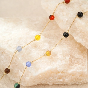 Golden stainless steel necklace with multi-colored beads on a white stone background