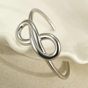 Detailed close-up of a silver infinity open bangle on a ceramic aesthetic background