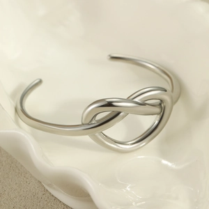 Silver stainless steel open bangle with multilayer love knot design on ceramic tray