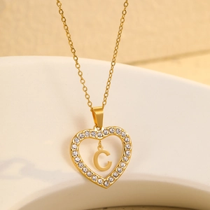 Detail of golden heart pendant with crystal border and letter C on stone background