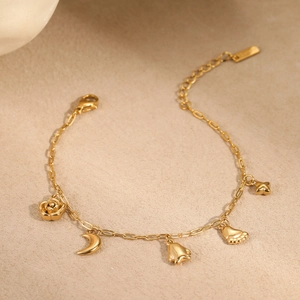 Détail d'un bracelet doré avec pendentifs rose, lune et étoile sur une surface beige