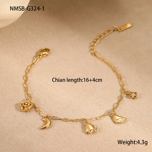 Détail d'un bracelet doré en acier inoxydable avec cinq breloques sur un fond de sable beige