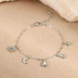 Bracelet en acier inoxydable argenté avec breloques rose, lune et étoile sur fond sable