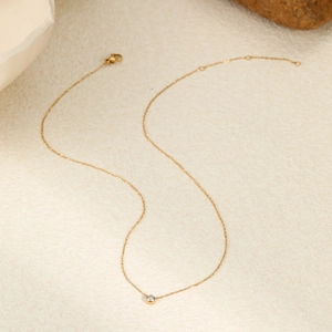 Collana minimalista in acciaio al titanio dorato con ciondolo in zircone tondo su base beige
