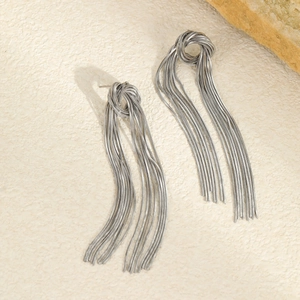Detailed view of silver snake chain tassel earrings with knot design on stone surface