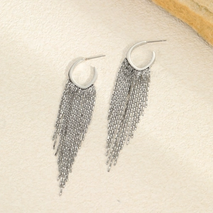 Detail view of long stainless steel tassel earrings on a textured natural stone background