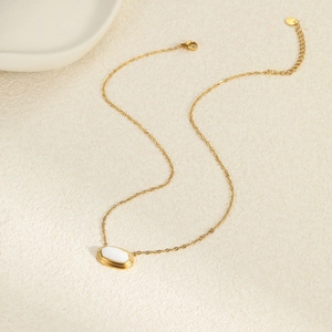 Detail van een 18K vergulde ketting met een witte ovale edelsteen hanger op zandstructuur