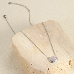 Detailopname van de zilveren ketting met lichtroze steen op een natuursteen