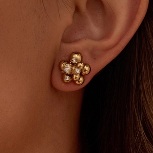 Close-up of gold flower stud earrings with clear zircon stones worn on the ear
