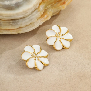 Detalle de pendientes de flores de esmalte blanco con borde dorado sobre arena de playa