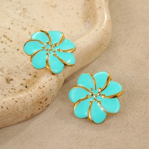 Detalle de pendientes de flores en esmalte azul con bordes dorados sobre bandeja de piedra