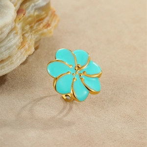 Elegante anillo de flor bañado en oro con esmalte turquesa sobre fondo de piedra texturizada