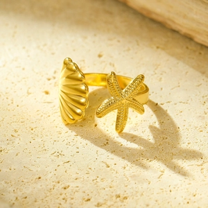 Vista macro dell'anello dorato con stella marina e conchiglia su sfondo naturale