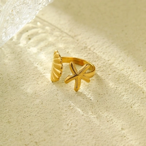 Dettaglio dell'anello dorato con stella marina e conchiglia su sfondo di sabbia