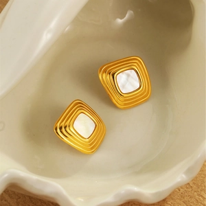 Detailansicht quadratischer Goldohrstecker mit Perlmutteinlage auf einer Muschelschale