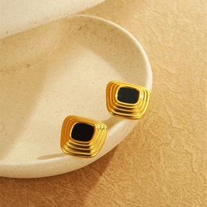 Makroaufnahme goldener quadratischer Ohrstecker mit schwarzem Achat auf Keramikschale