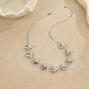 Détail du collier à pendentifs cœur argentés sur fond de sable au style cadeau chic