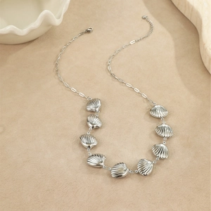 Détail du collier argenté avec pendentifs coquillages texturés sur une surface beige mat