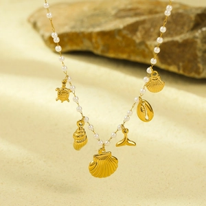 Detailed view of ocean-themed necklace with turtle, shell and pearl charms on sea sand