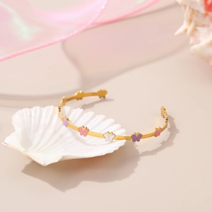 Detail of gold butterfly open bangle with colorful enamel charms on white seashell