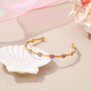 Detail view of a gold-plated C-shaped bracelet featuring colorful purple enamel butterflies