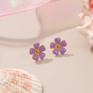 Detail view of purple floral earrings with gold trim on a shell and tulle background